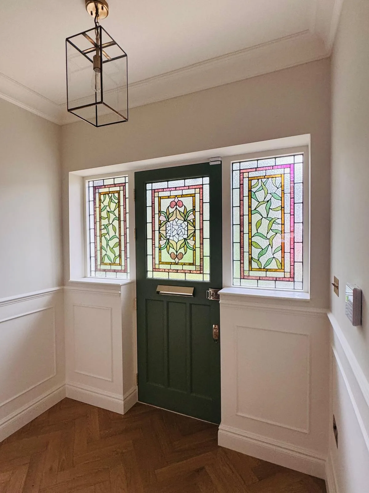 Hallway view of the completed Accoya entrance door and stained glass side windows with herringbone flooring