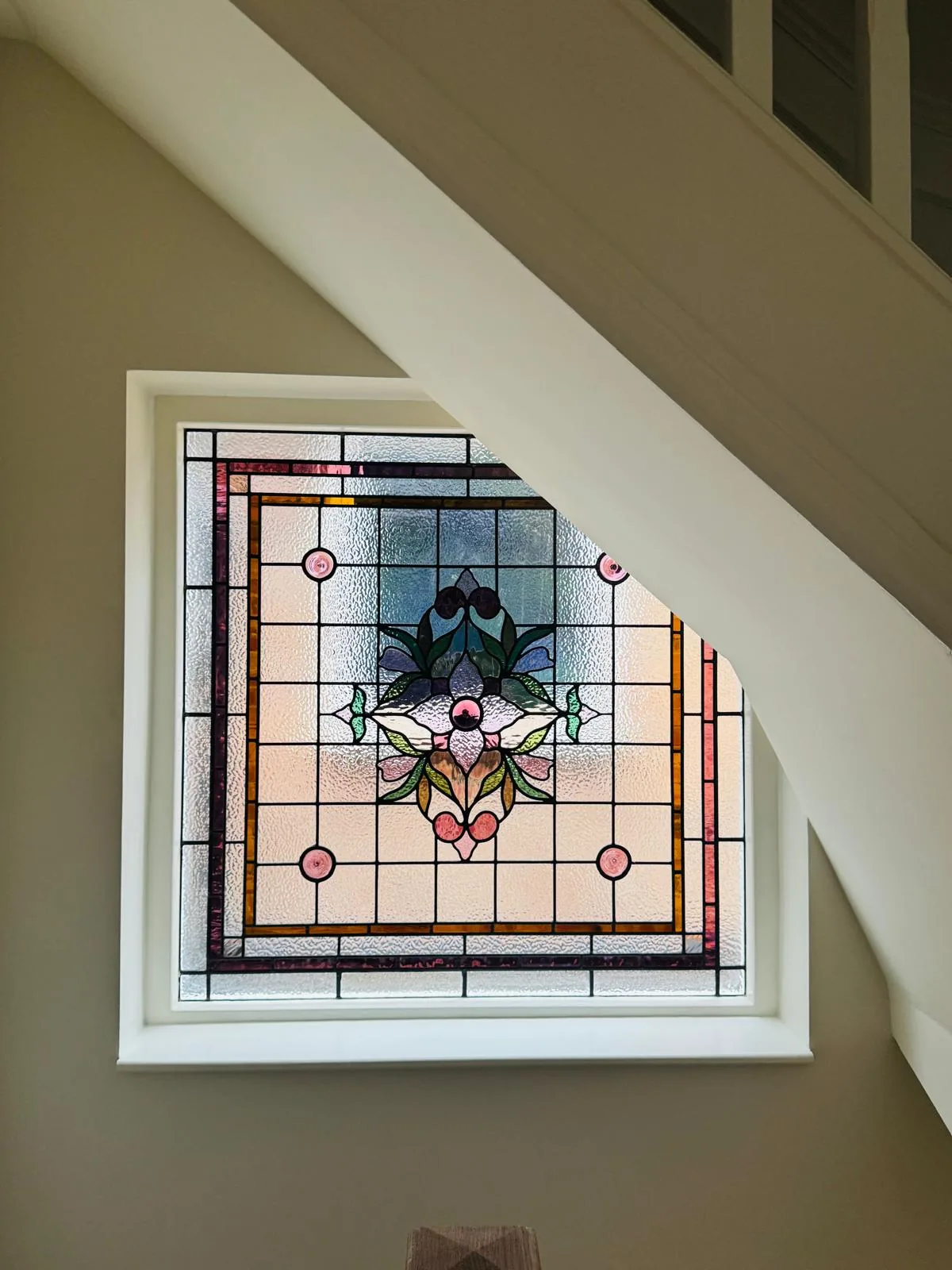 Bespoke stained glass staircase window with geometric grid and central floral motif