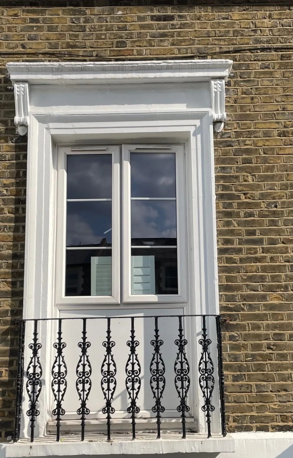 The PVC window being replaced, set in the original stucco surround with cast iron balcony