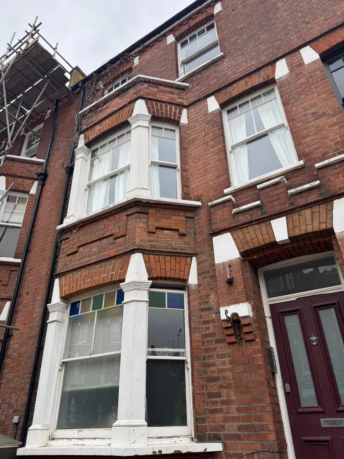 Victorian terrace in Islington before sash window replacement, showing paint failure on the cills and original stained glass in the ground floor bay